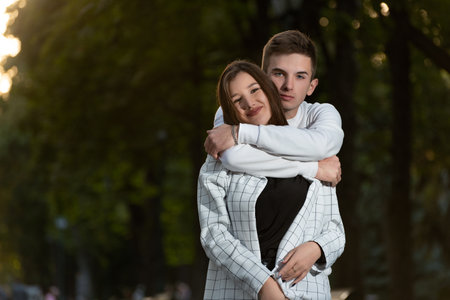 Portrait of loving young couple in park. Guy hugs girls shoulders.の写真素材