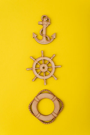 Wooden anchor, steering wheel and lifebuoy on yellow background. Vertical frame.