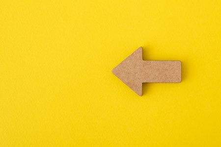 Wooden arrow on yellow background. Direction indicator. Copy space. Mock up.