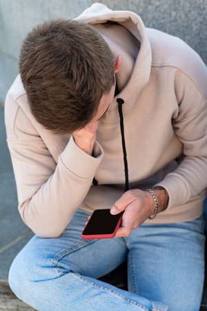 Guy sitting and holding phone. Portrait of man with smartphone in his hands. Vertical frame.の写真素材