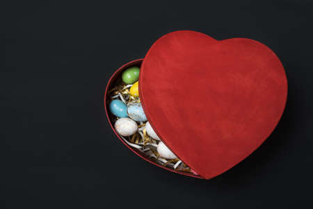 Red semi open Heart shaped box with colorful Easter eggs. Black background. Top view