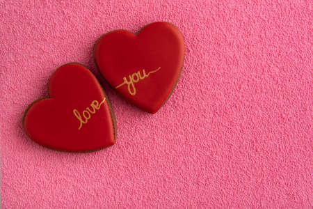 Two red cookies in shape of hearts with the inscription Love uoy on pink background. Copy space