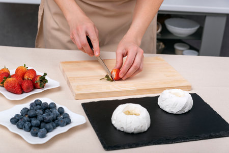 Pastry chef cuts strawberries to make meringue fruit cakes. Hands of confectioner.の写真素材