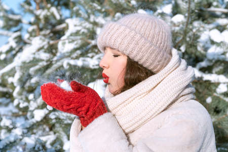 Girl is holding the snow and blowing on it. Portrait of young woman in winter hat.の写真素材