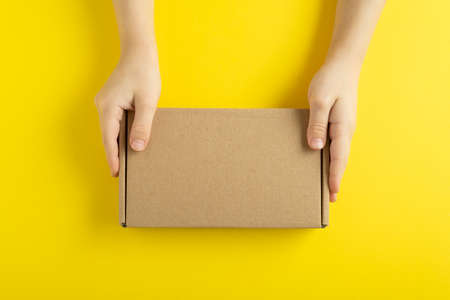 Cardboard box in hands on yellow background top view. Copy space. Mock up