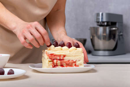 Confectioner woman decorates cake with berries. Vanilla cream cake with berry filling.の写真素材