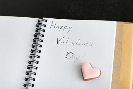 Handwritten inscription in notebook Happy Valentines Day and cookies in the shape of heart