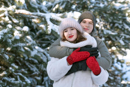Young couple with love huggins against snowy forest background. Winter holidays.の写真素材