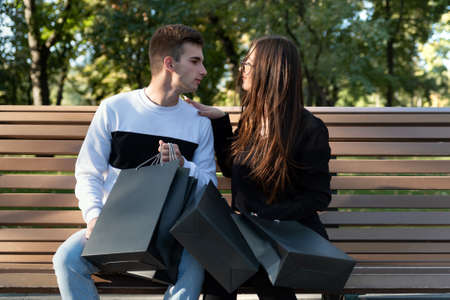 Guy and girl are sitting on bench after shopping with many packages.
