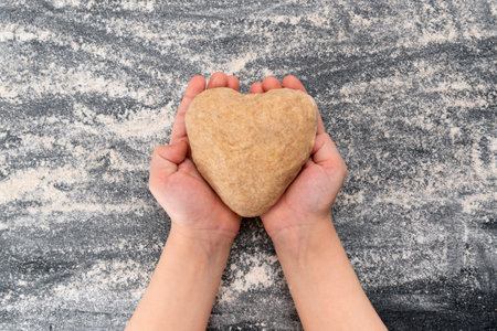 Child holds a dough in shape of heart. Homemade cookies with love.