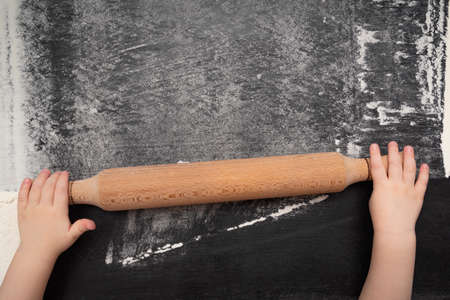 Childrens hands with a wooden rolling pin. Surface with flour. Top view.