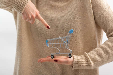 Small shopping cart on female hand. Finger points to trolley cartの写真素材