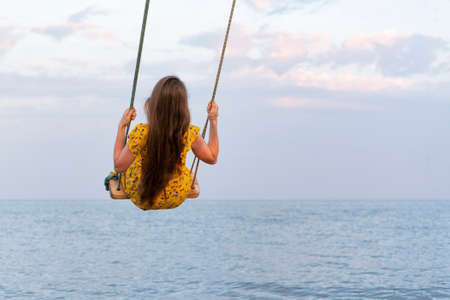 Young woman with long hair is riding a swing above the water. Keep calm.の写真素材