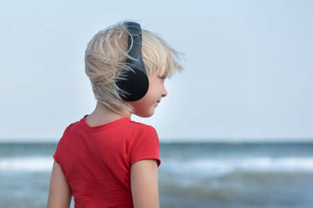 Portrait of fair-haired boy in headphones on sea background. Side viewの写真素材