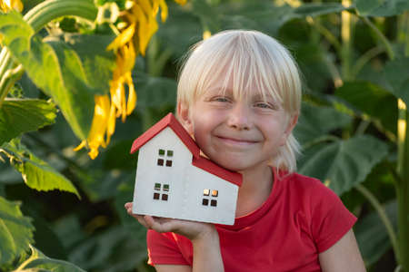 Fair-haired boy with small house is surrounded by field of sunflowers. Eco-friendly home. Green housesの写真素材