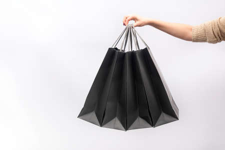 Female hand holds black paper shopping bags isolated on white backgroundの写真素材