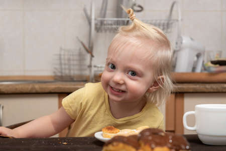 Cheerful blonde girl in the kitchen eats cookiesの写真素材