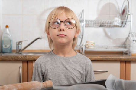 Portrait of blond boy with glasses in the kitchen. Pensive boy.
