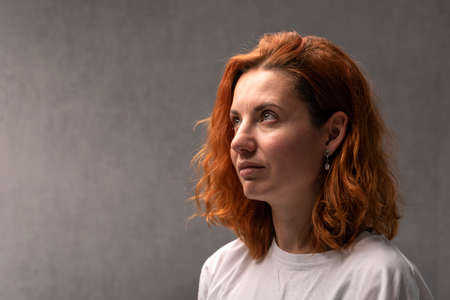 Portrait of red-haired woman on gray background side view