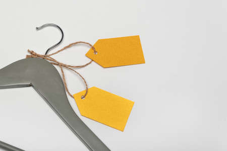 Gray coat hanger with yellow paper labels. White background. Blank label, mockup. Clothing tag.の写真素材