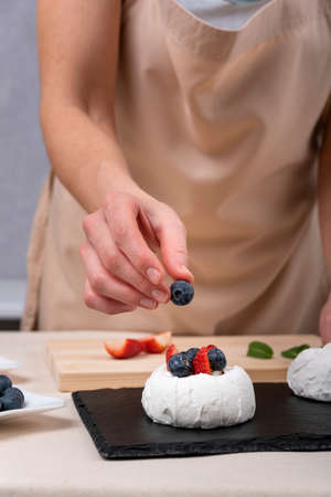 Confectioner decorating meringue with blueberries and strawberry. Process of making cakes.の写真素材