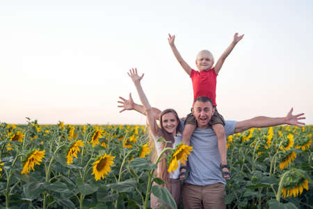 Young family stands on field of sunflowers with their hands up. Happy family. Rural vacation.の写真素材