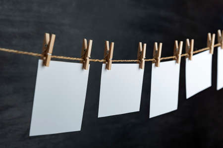 White blank paper notes hang with clothespins on rope. Black background. Copy spaceの写真素材