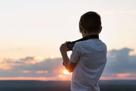 Boy photographs the sunset. Child with camera on setting sun backgroundの写真素材