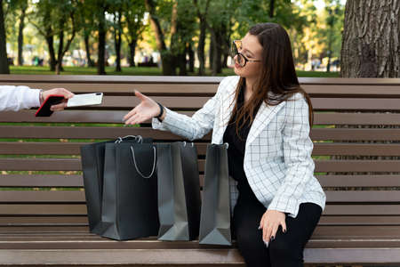 Woman shopper with shopping bags stretches out her hand for the phone. Cashback for purchasesの写真素材
