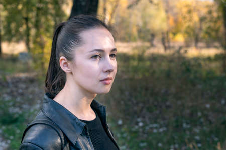 Portrait of girl on park background. Beautiful brunette young woman thoughtfully looks straight....