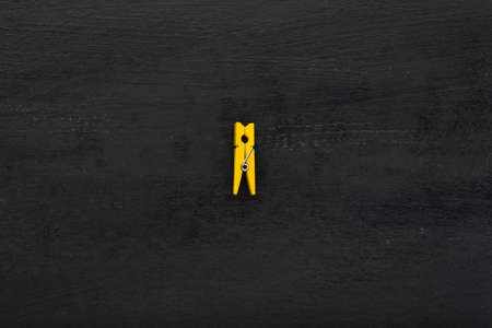 Single yellow wooden clothespin on a black background. Loneliness concept. Copy space.