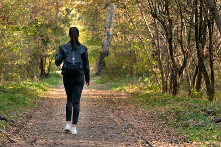 Young woman is walking along the autumn alley of the park. Back view.の写真素材