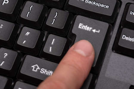 Finger presses the Enter button. Black keyboard close up.の写真素材