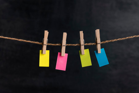 Small blank multicolored paper hang with clothespins on rope on black background. Copy space. Place for your textの写真素材