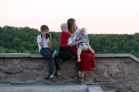 Young mother with three children is resting near forest. Traveling with children. Happy family.の写真素材