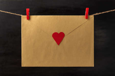 Envelope with heart hanging with clothespins on rope string peg. Letter for loved ones. Valentine's Day. Black background.の写真素材