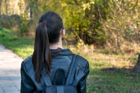 Girl with ponytail is walking in the park. Young girl student stands in the park. Back viewの写真素材