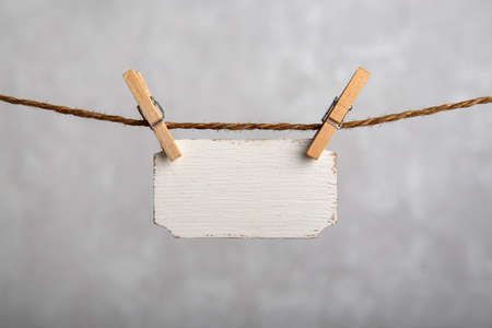 Small nameplate hanging with clothespins on rope. Blank white sign, plate for an inscription. Copy space. Place for text.の写真素材