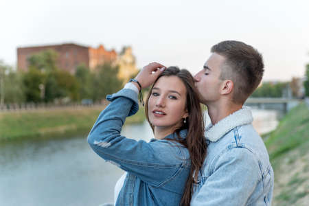 Guy gentle kisses his beloved on the head. Portrait of young loving couple on river. Romantic date.の写真素材