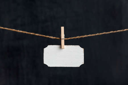 Small nameplate.Blank wooden sign hang with clothespins on rope on black background. Copy spaceの写真素材