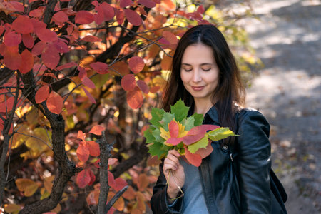 Dark-haired girl in park holding bouquet of autumn leaves. Beautiful young woman in the forest....