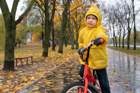 Portrait of boy in yellow raincoat on bicycle on autumn park background. Child riding bicycle in the rain.の写真素材