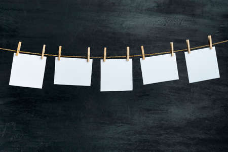 Blank paper notes hang with clothespins on rope. Black background. Copy space.