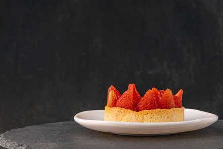 Tartlet with fresh strawberries on saucer on black background. Side view. Fruit cake. Copy space,の写真素材