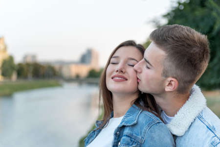 Portrait of young loving couple on river. Guy kisses his beloved on the cheek. Romantic date.の写真素材
