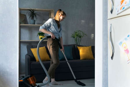 Young woman is cleaning the apartment with vacuum cleaner. Housekeeper vacuums the living roomの写真素材