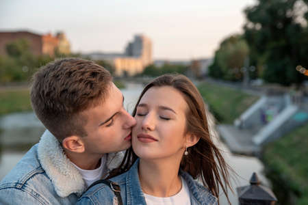 Portrait of beautiful young couple. Guy gently kissing his beloved. Happy girl closed eyes. Romantic date in city.の写真素材