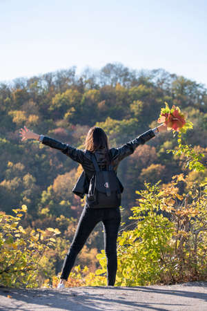 Beautiful girl on autumn park background. Girl holds bouquet of leaves and enjoys warm day. Back...