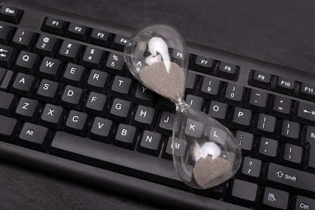 Hourglass on computer keyboard. Time management concept. Urgency and outcome of time