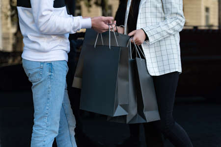 Man and woman are holding black shopping bags. Girl and guy meet after shopping. Mock up. Black friday concept.の写真素材